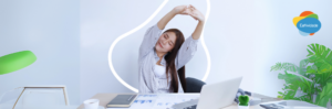 Mulher em uma estação de trabalho ergonômica, sorrindo e com a postura correta, exemplificando a importância da ergonomia no trabalho.