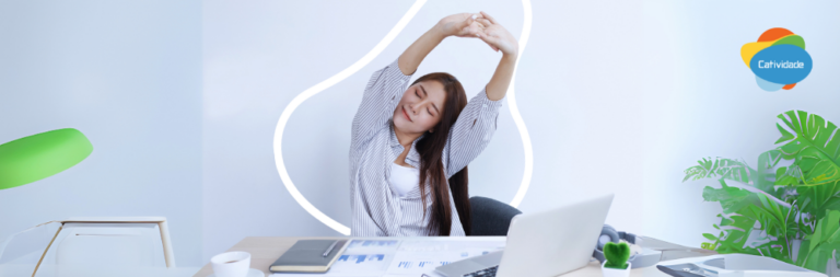 Mulher em uma estação de trabalho ergonômica, sorrindo e com a postura correta, exemplificando a importância da ergonomia no trabalho.